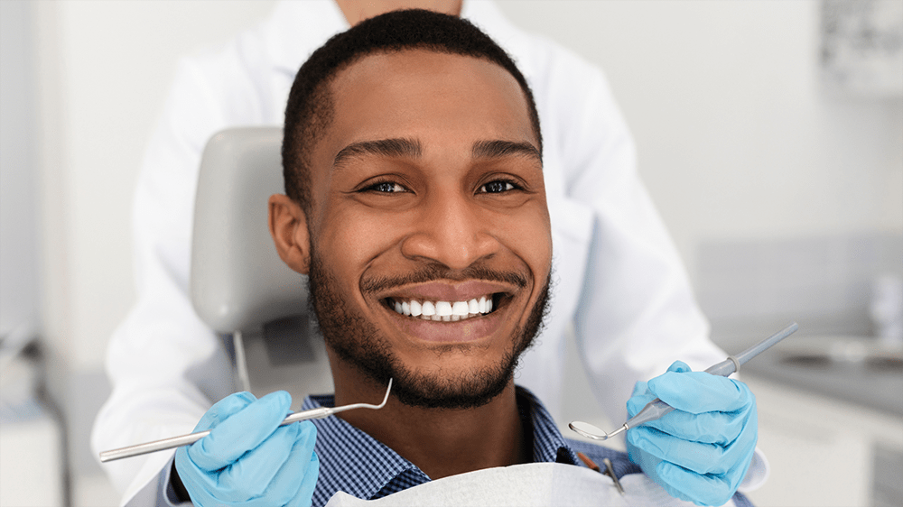 A man smiling in a dental chair while a dentist holds tools beside him
