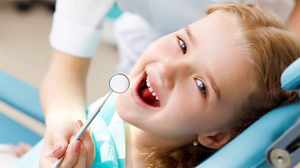 Young girl smiling with mouth open while dentist holds a dental mirror