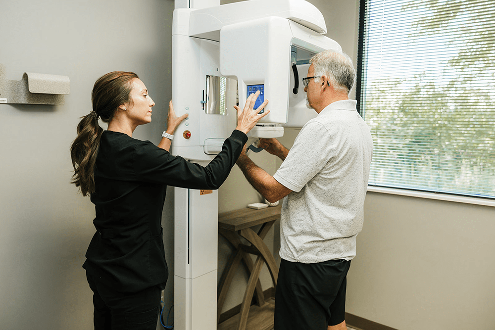 A female dental assistant adjusting a panoramic X-ray machine for an older male patient