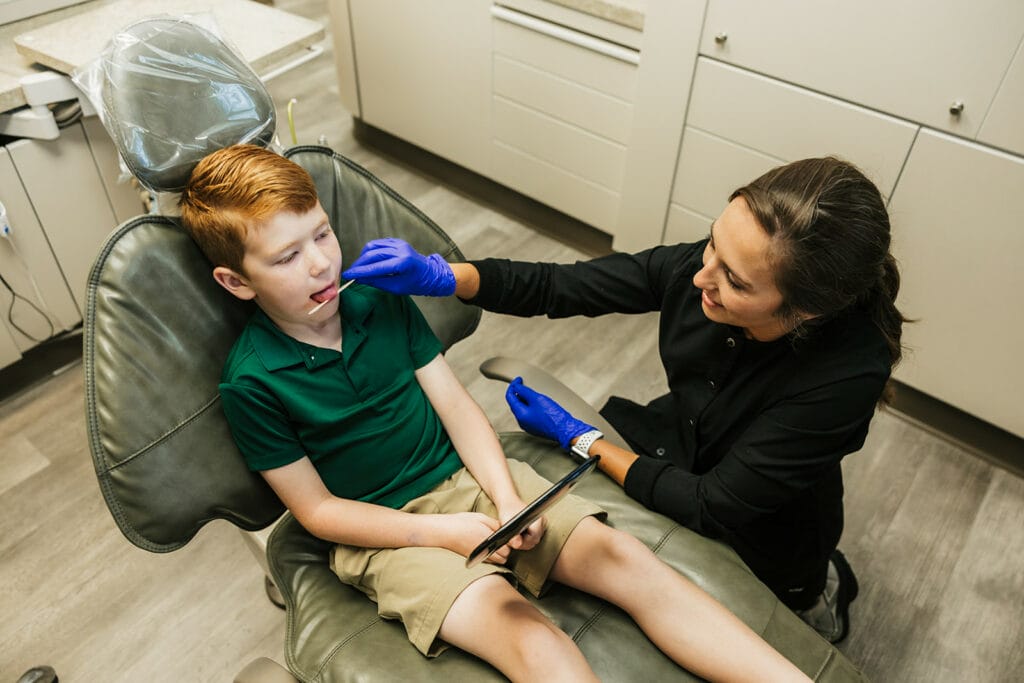 Dental assistant examining a young boy’s mouth in a dental chair
