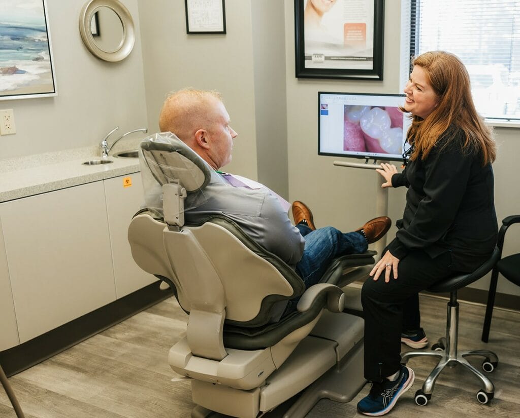 Dentist showing a male patient a dental image on a screen in an exam room