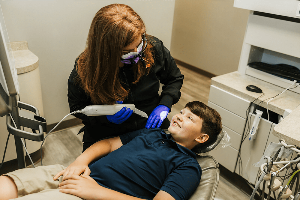 A female dentist scanning a boy's teeth while he lies in a dental chair, both smiling