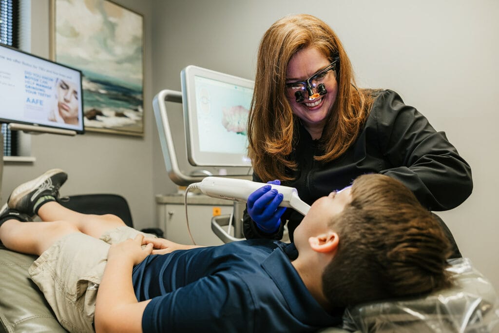 A female dentist using an intraoral scanner on a boy lying in a dental chair