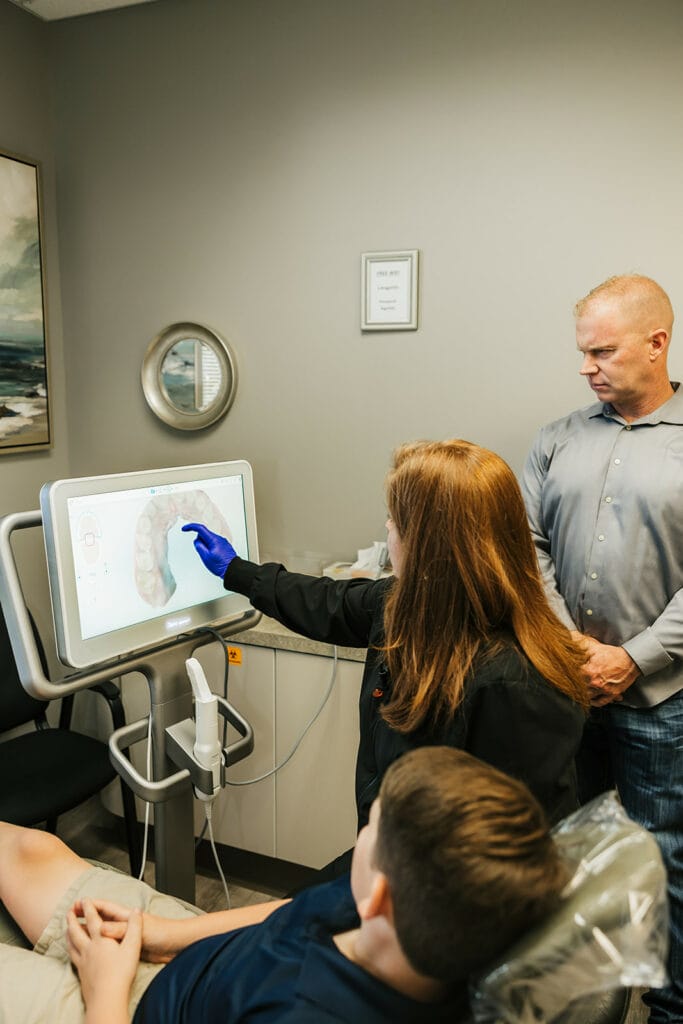 A dentist explaining a digital dental scan to a young male patient and an adult standing nearby