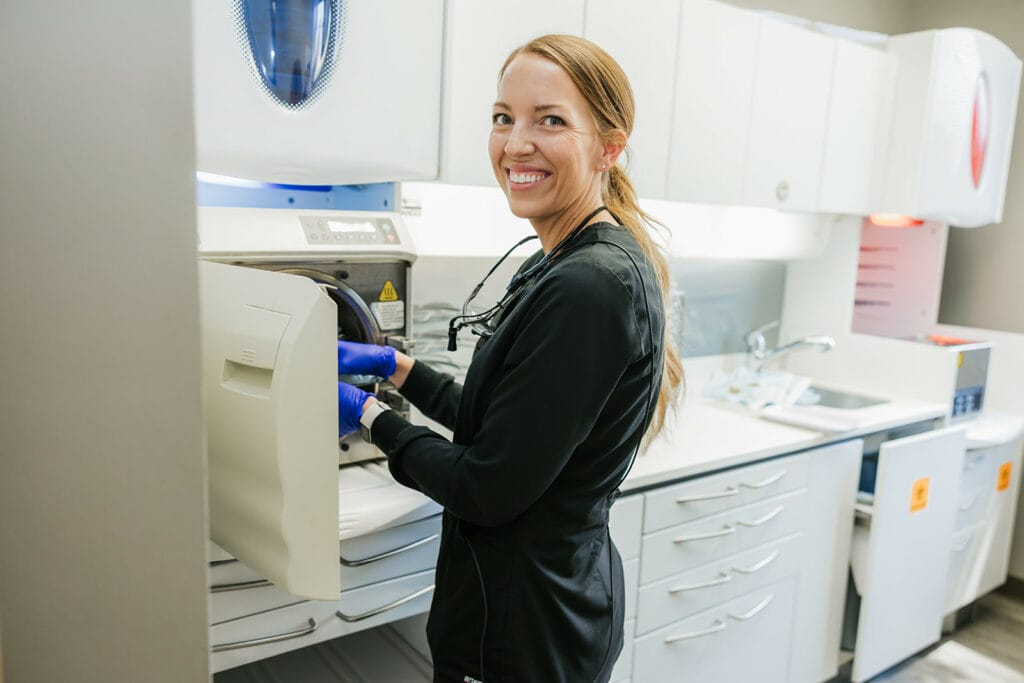 A smiling dental assistant operating a sterilization machine in a clean, modern clinic
